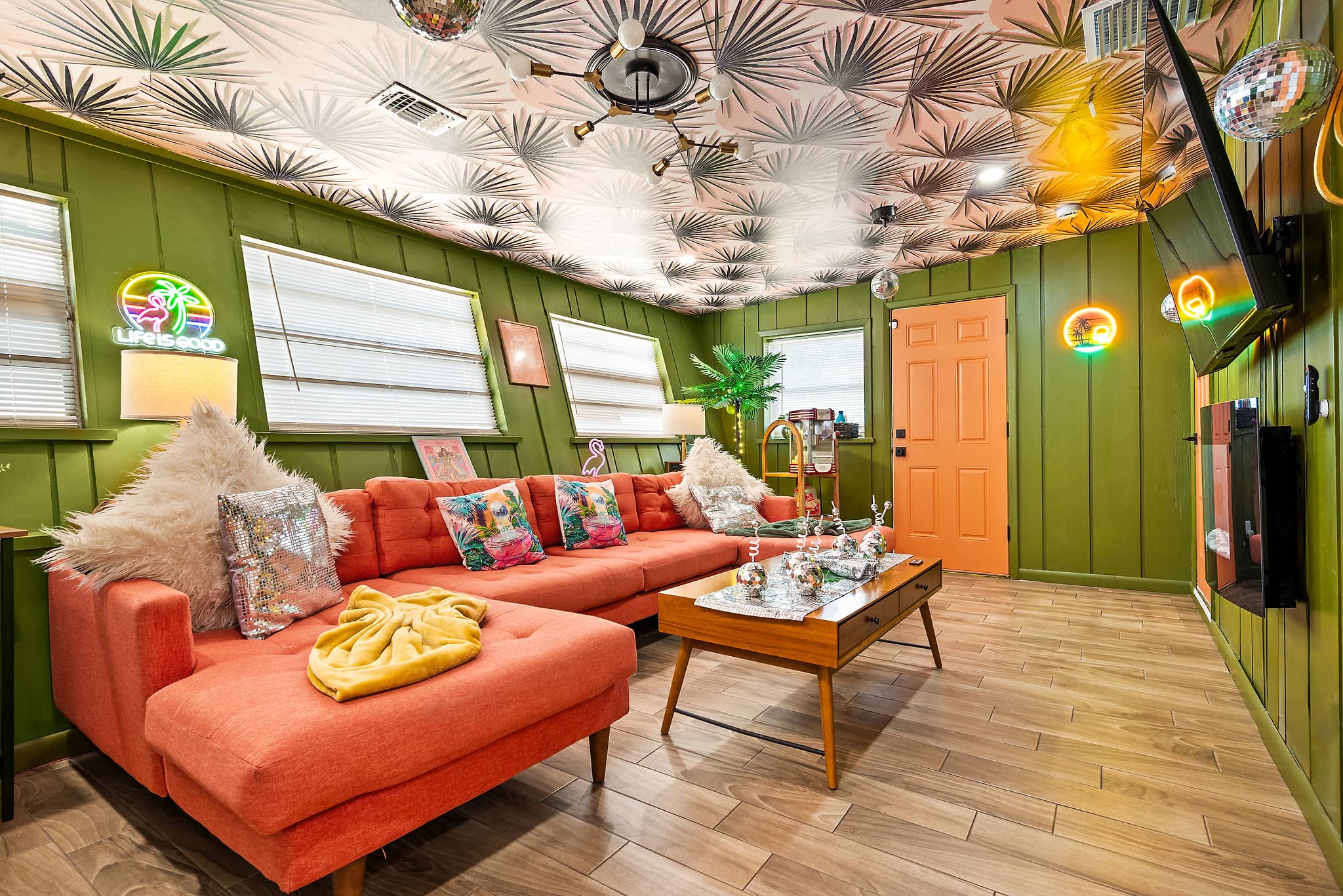 Retro 70s disco lounge with coral sectional sofa, palm-pattern ceiling, disco ball and neon sign at Tropical Disco vacation rental St. Petersburg FL